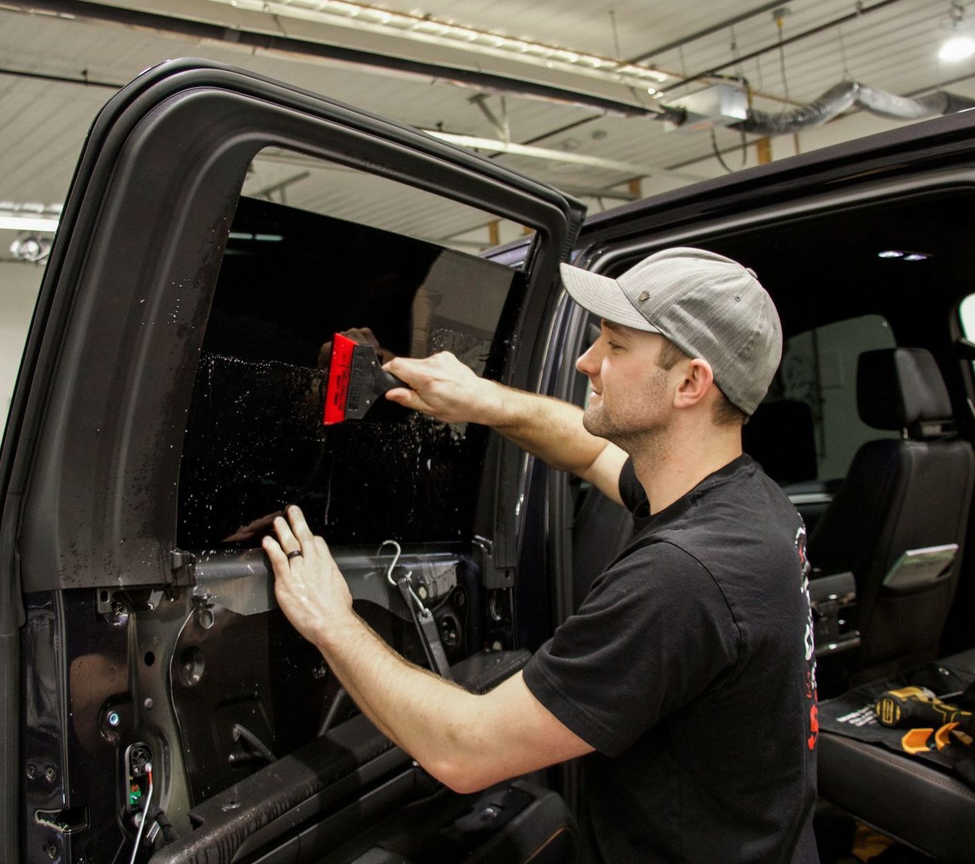 A man in a baseball cap is working on a truck window