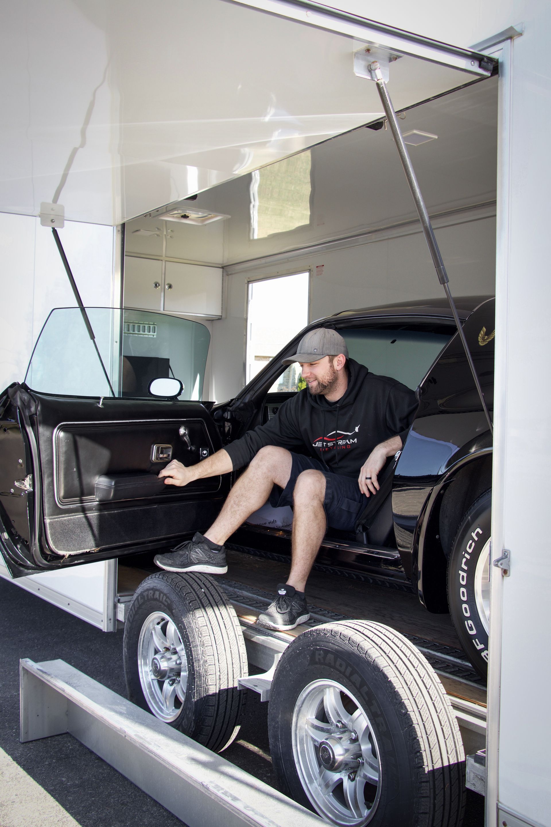 A man is sitting in the back of a car trailer.