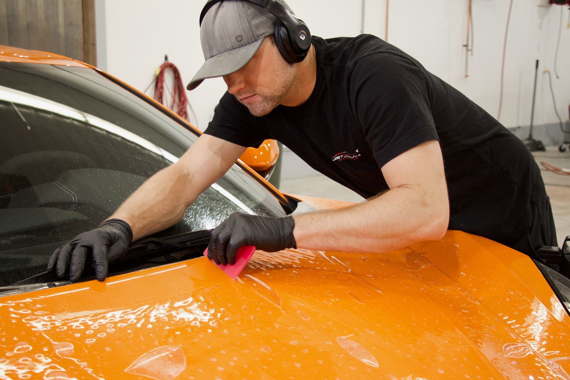 Detailer polishing a black car hood with a buffer in a garage