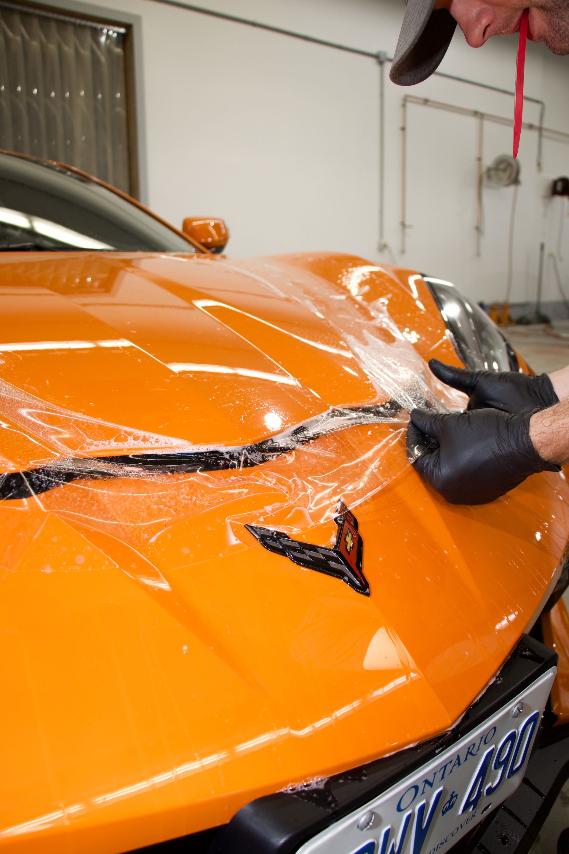 Orange sports car being wrapped in clear protective film in a garage