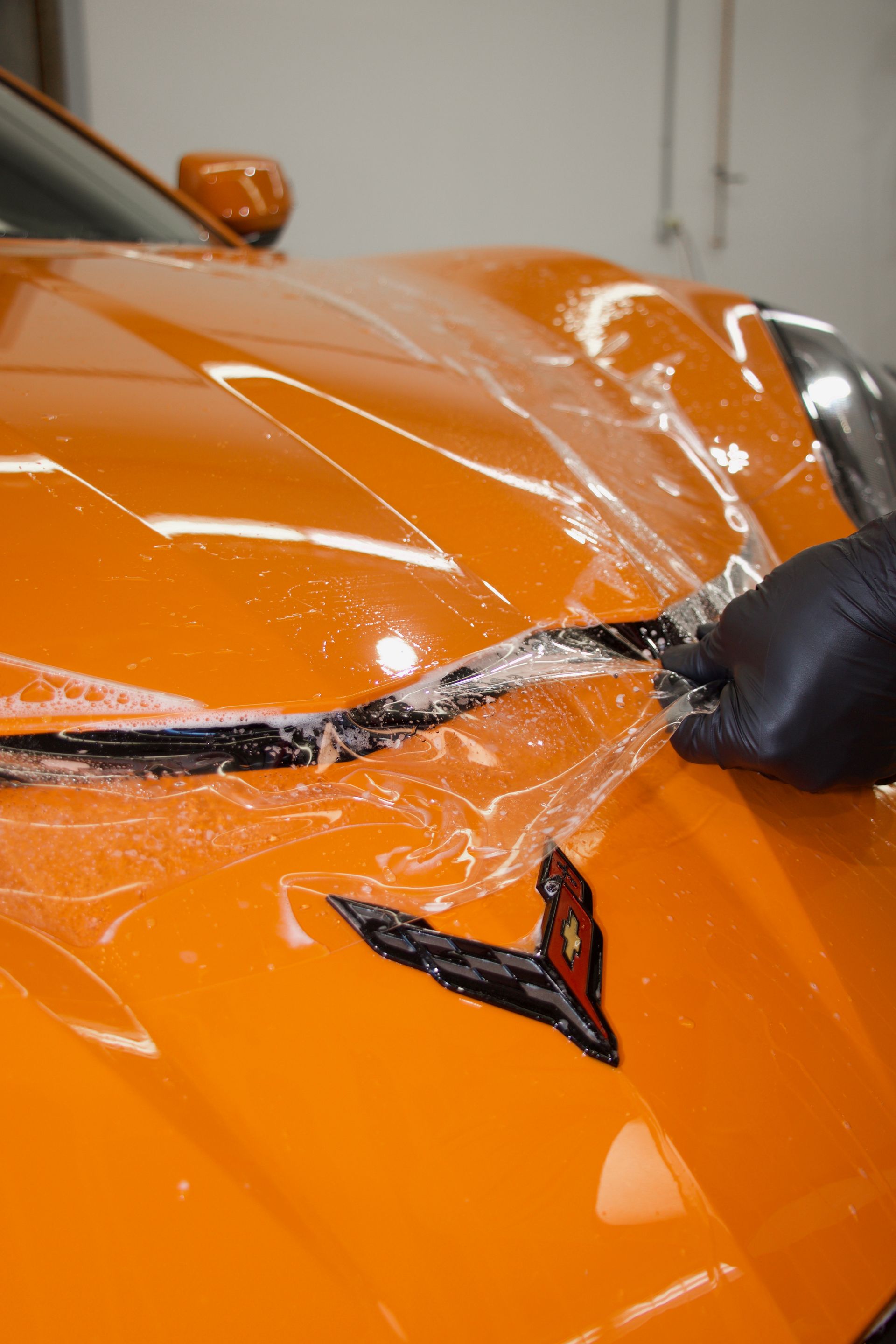 Close-up of an orange sports car with a crushed hood and shattered windshield being repaired