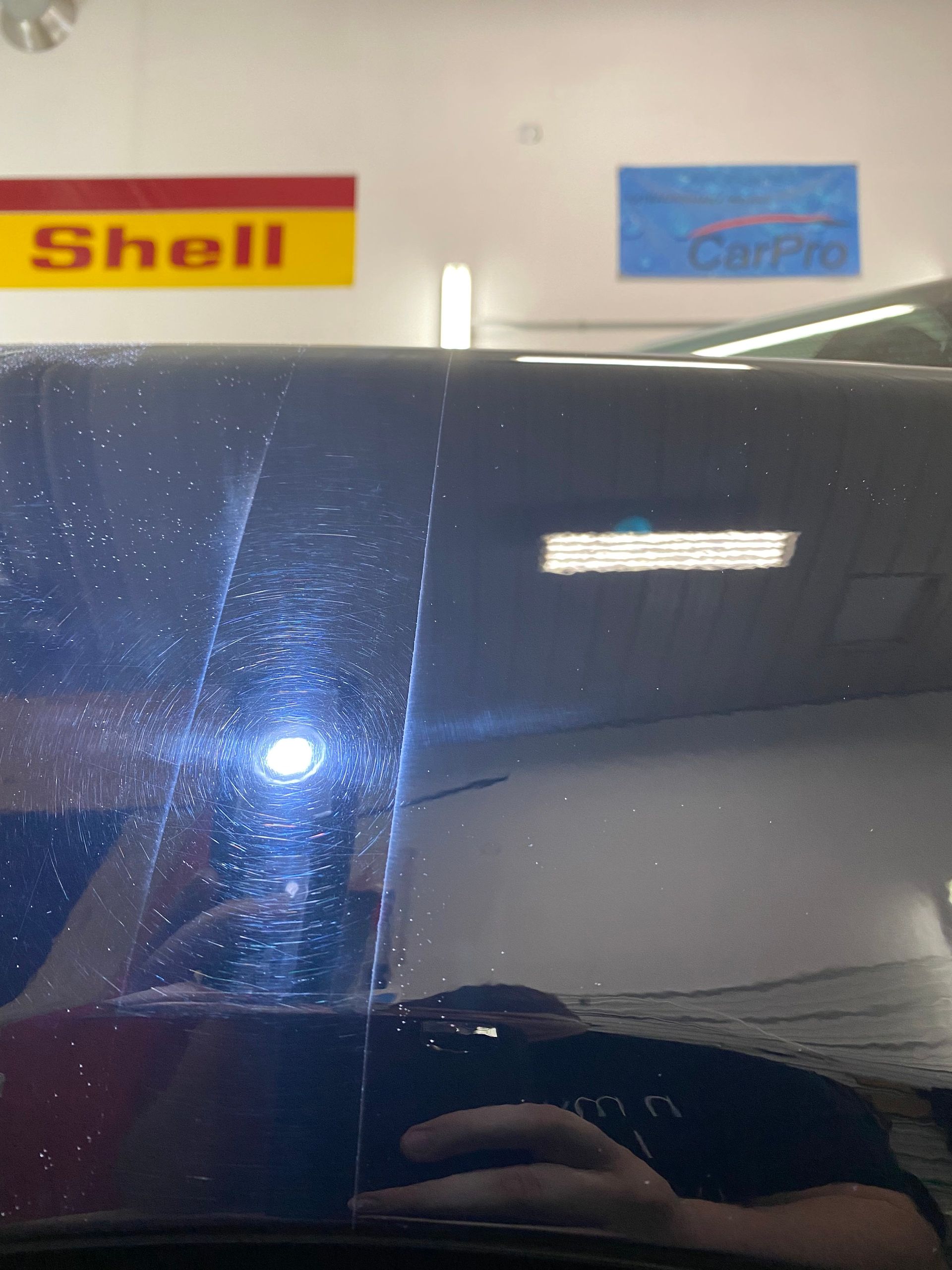 Dark blue car reflecting ceiling lights in a garage, with Shell and Corvette signs above.