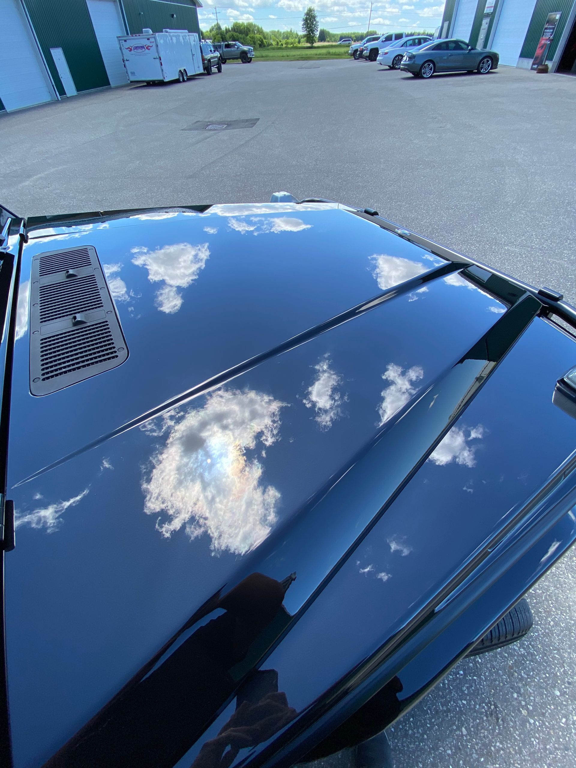 A black car is parked in a parking lot with a reflection of clouds in the hood.