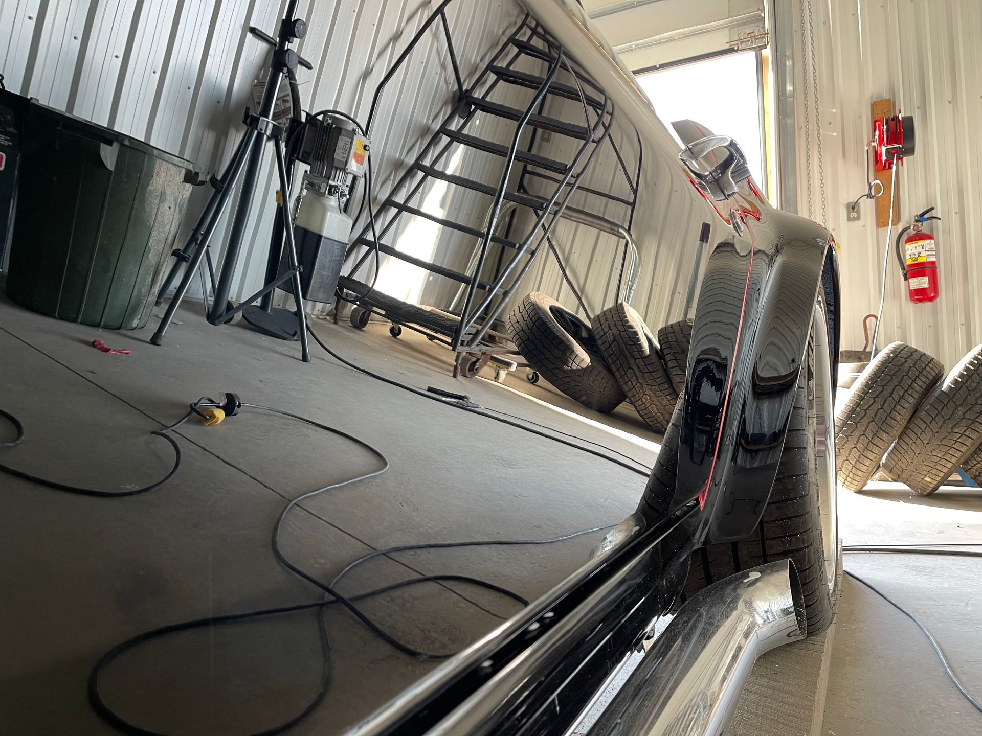 Curved black-and-silver race car in a garage, with a ladder and cables on the floor.