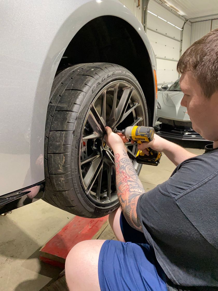 A man is working on a car wheel with a drill.