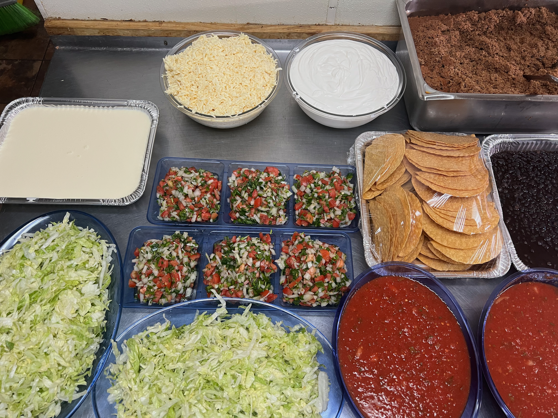 A table with various taco toppings: cheese, sour cream, meat, shells, beans, salsa, and chopped vegetables.