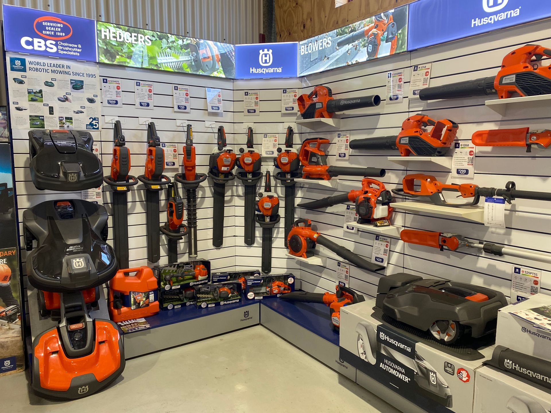 A Husqvarna tool display in a store, featuring blowers and robotic mowers in orange and black. — CBS Chainsaw & Brushcutter Specialists - HUSQVARNA in Wauchope, NSW