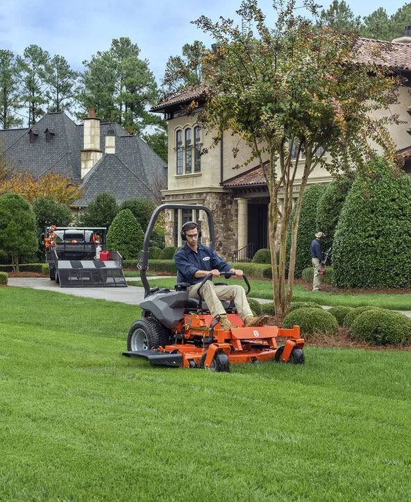 A Man Is Riding a Lawn Mower in Front of A House — CBS Chainsaw & Brushcutter Specialists - HUSQVARNA in Wauchope, NSW