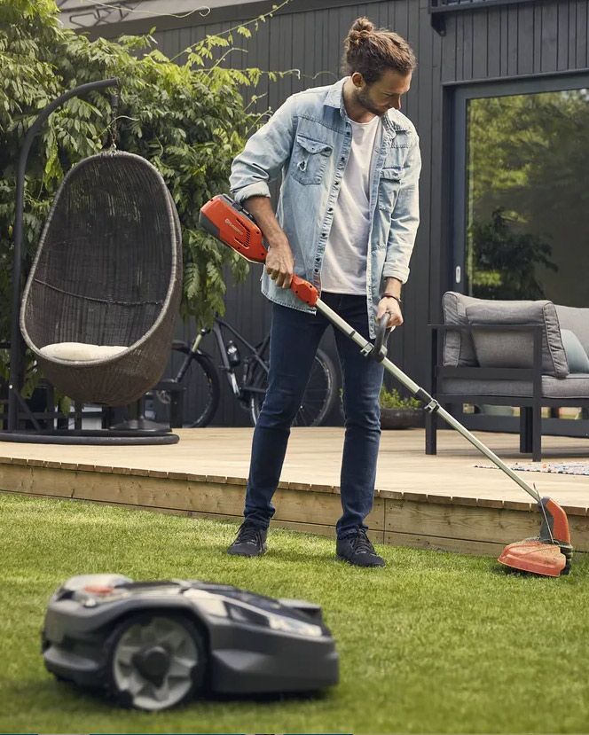 A Man Is Using a Robotic Lawn Mower to Cut the Grass — CBS Chainsaw & Brushcutter Specialists - HUSQVARNA in Wauchope, NSW