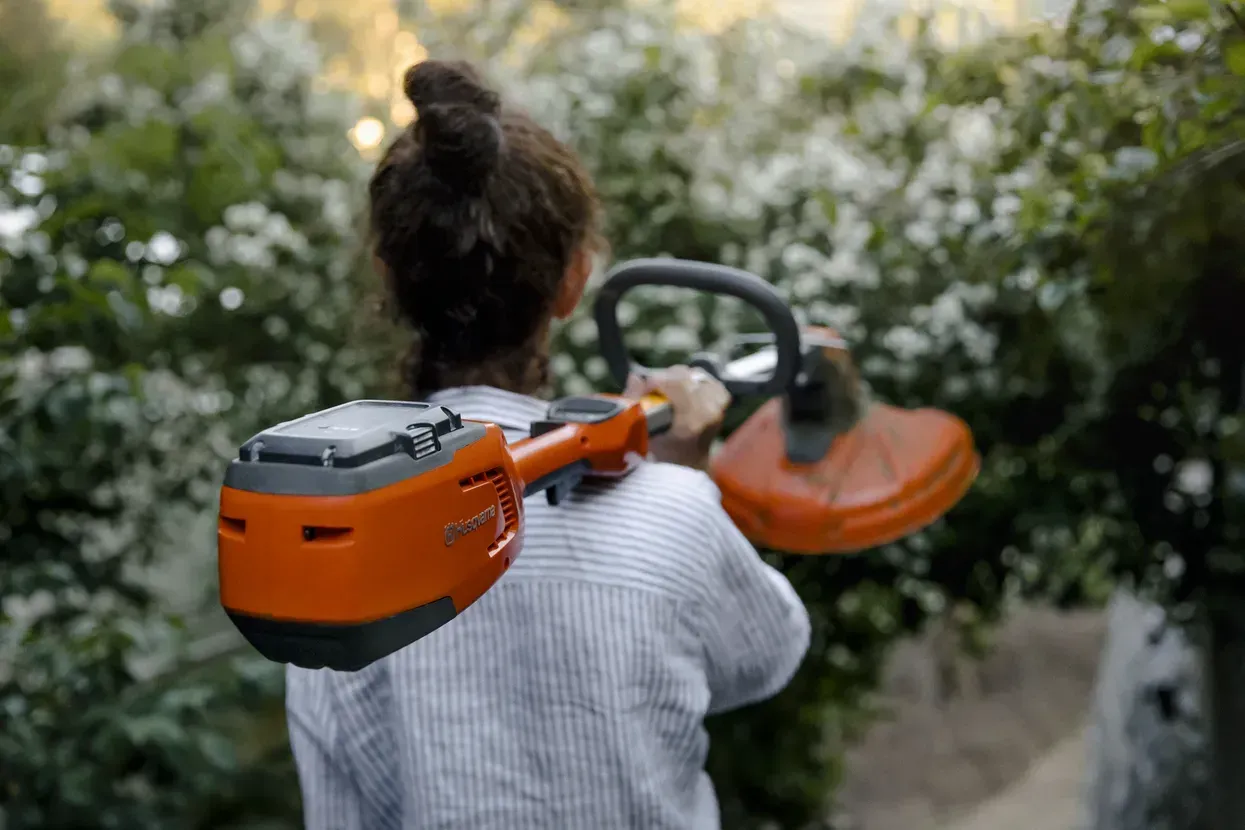 A Woman Is Holding a Lawn Mower on Her Shoulder — CBS Chainsaw & Brushcutter Specialists - HUSQVARNA in Wauchope, NSW
