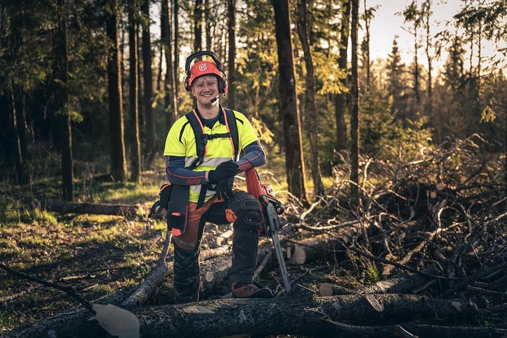 A Man Is Sitting on A Log in The Woods with A Chainsaw — CBS Chainsaw & Brushcutter Specialists - HUSQVARNA in Wauchope, NSW
