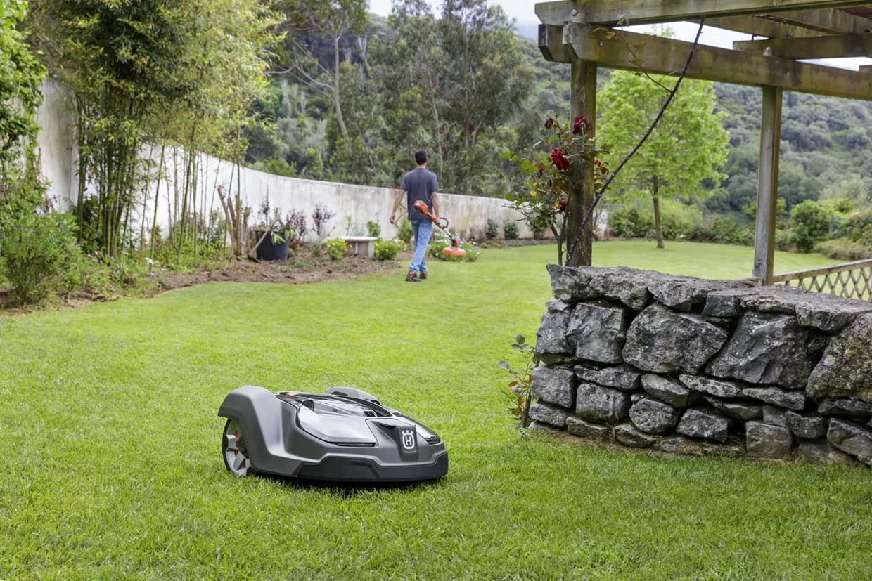 A Man Is Mowing a Lawn with A Robotic Lawn Mower — CBS Chainsaw & Brushcutter Specialists - HUSQVARNA in Wauchope, NSW