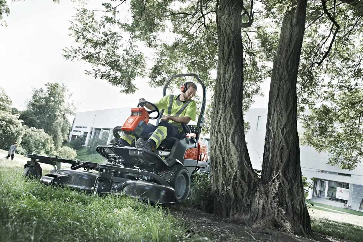 A Man Is Riding a Lawn Mower Next to A Tree — CBS Chainsaw & Brushcutter Specialists - HUSQVARNA in Wauchope, NSW