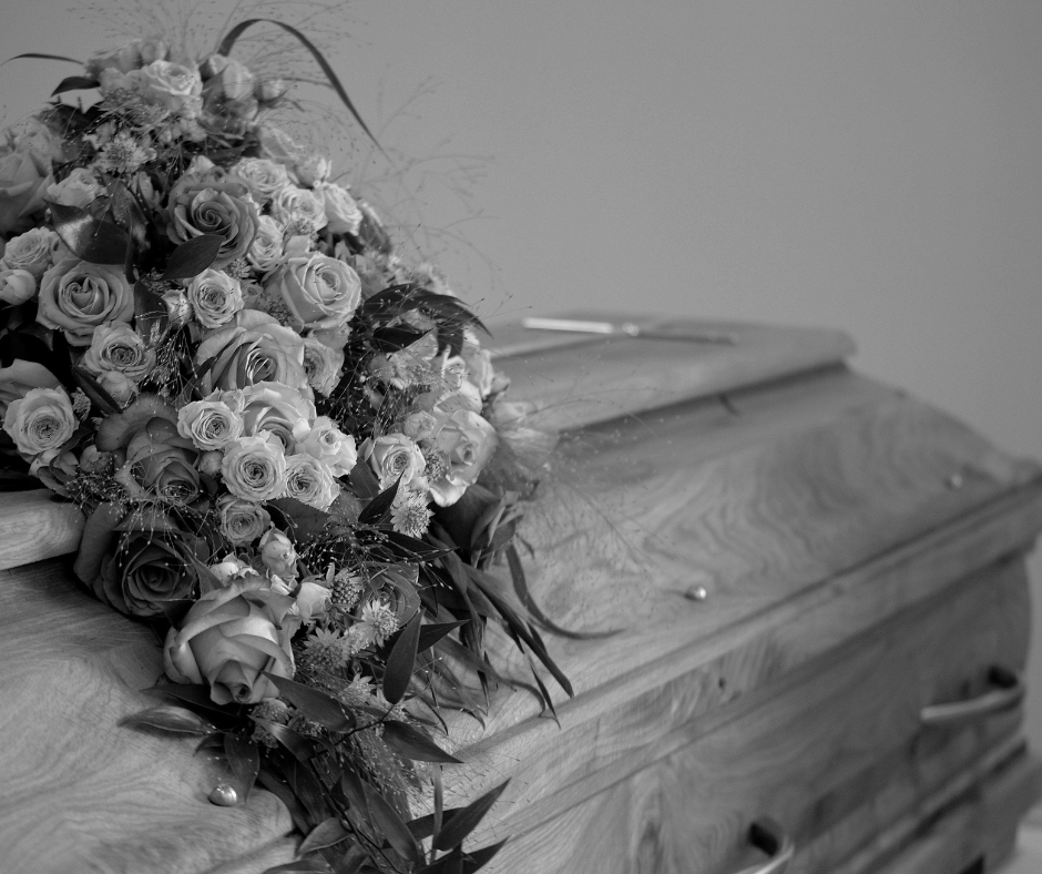 Black and white image of a wooden casket adorned with an elegant floral arrangement featuring roses