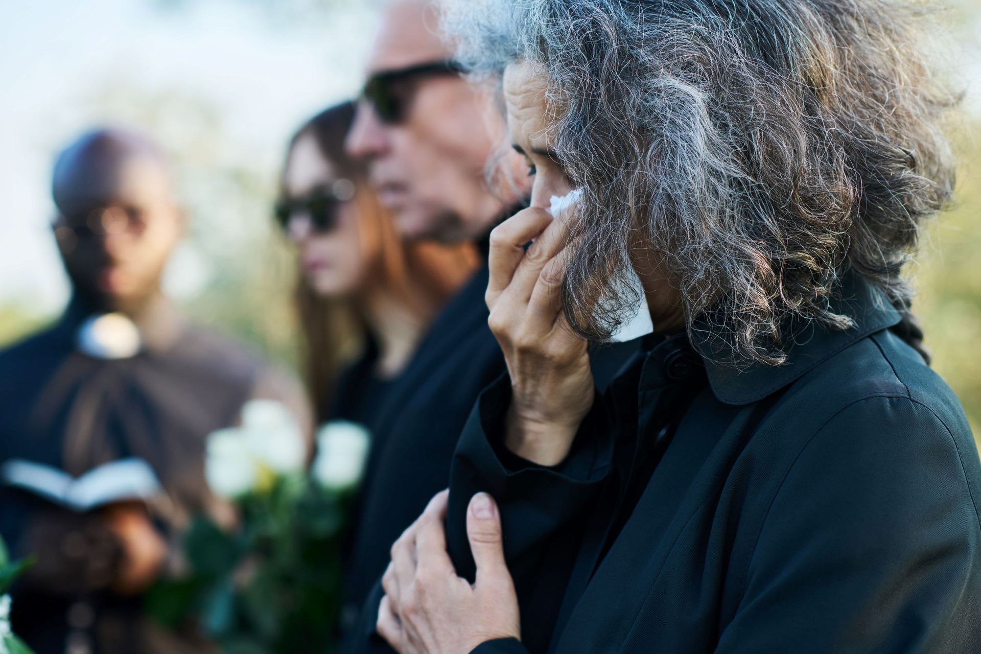 Senior woman with grey hair wiping tears with handkerchief at funeral