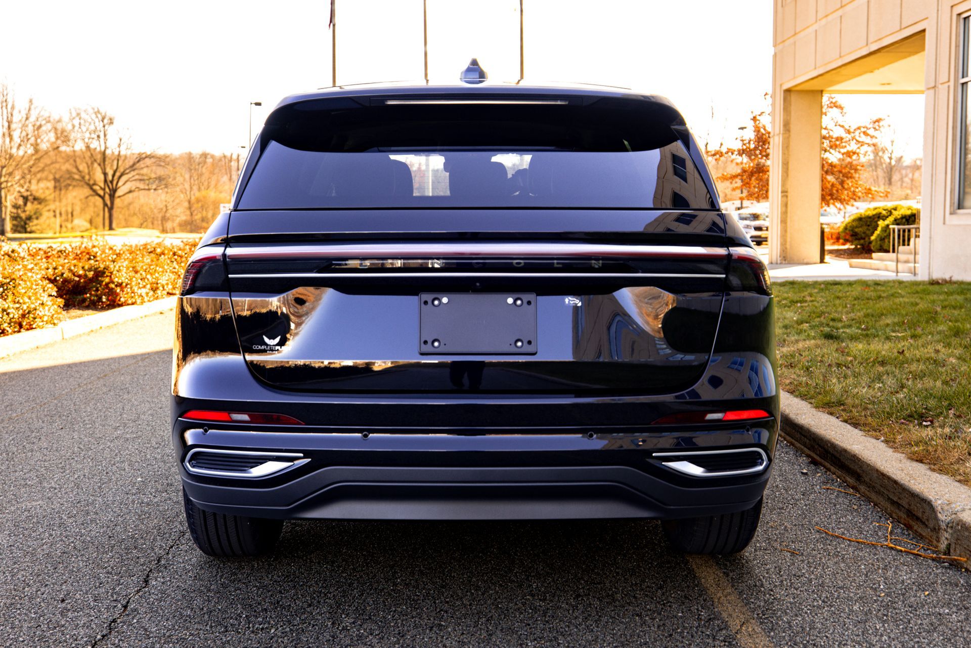 A black car is parked in a parking lot in front of a building.