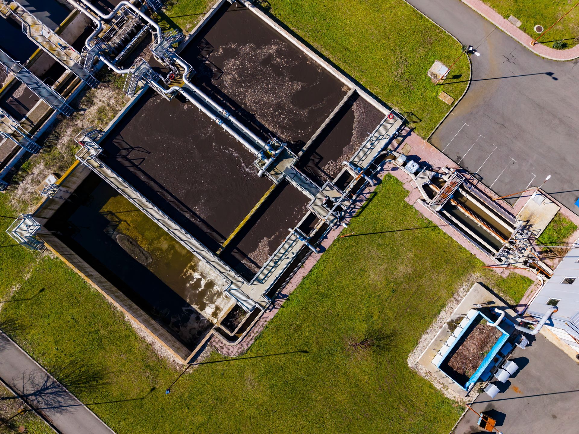Aerial view of an industrial water treatment facility with concrete tanks and pipes beside grass and a road