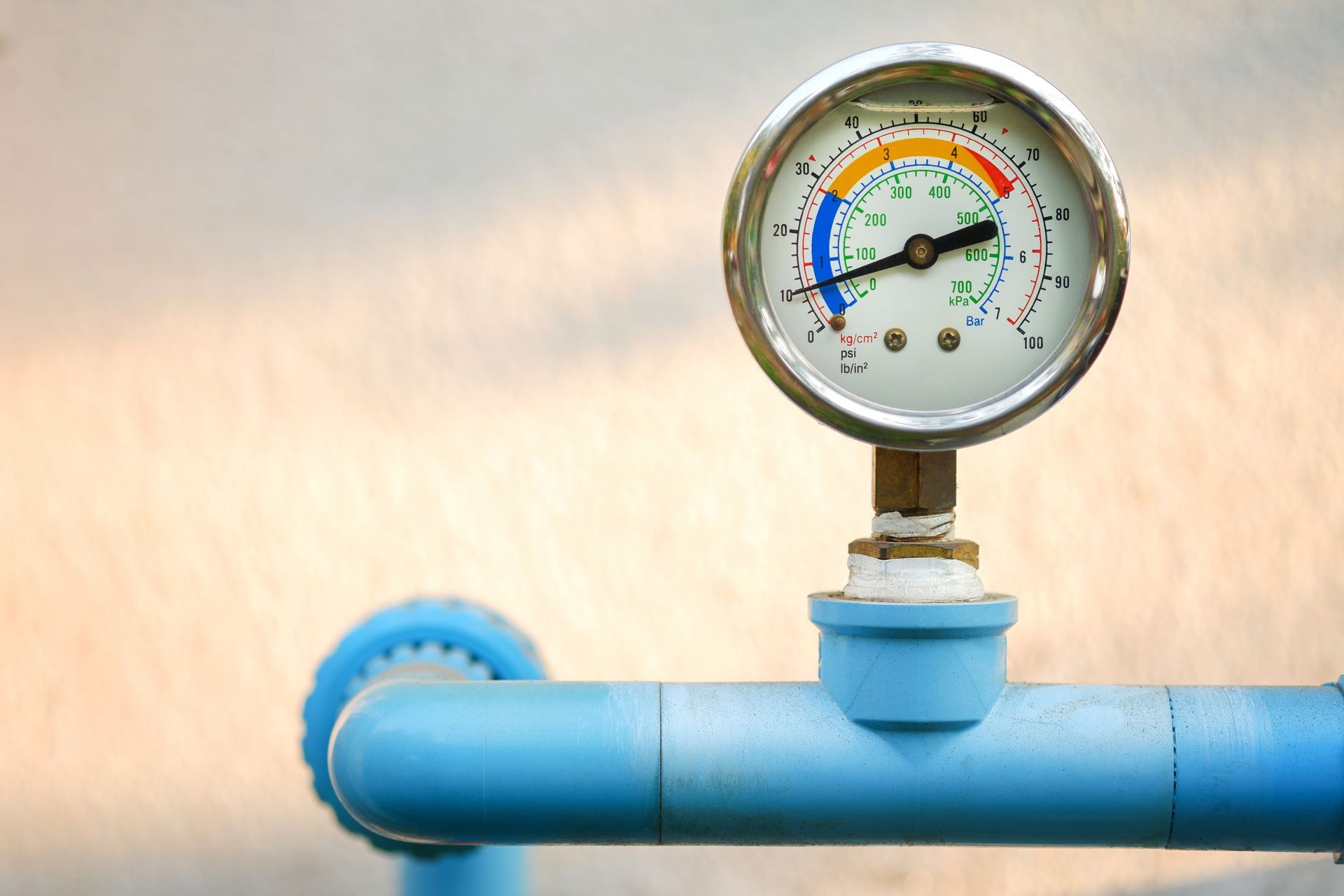 Pressure gauge on a blue pipe, showing measurements against a blurred light background