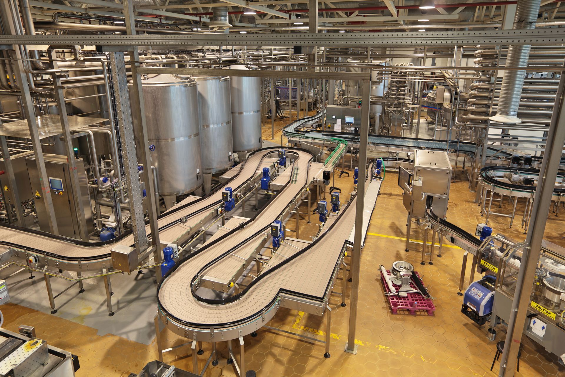 Industrial factory interior with conveyor belts, pipes, tanks, and workers on a polished floor