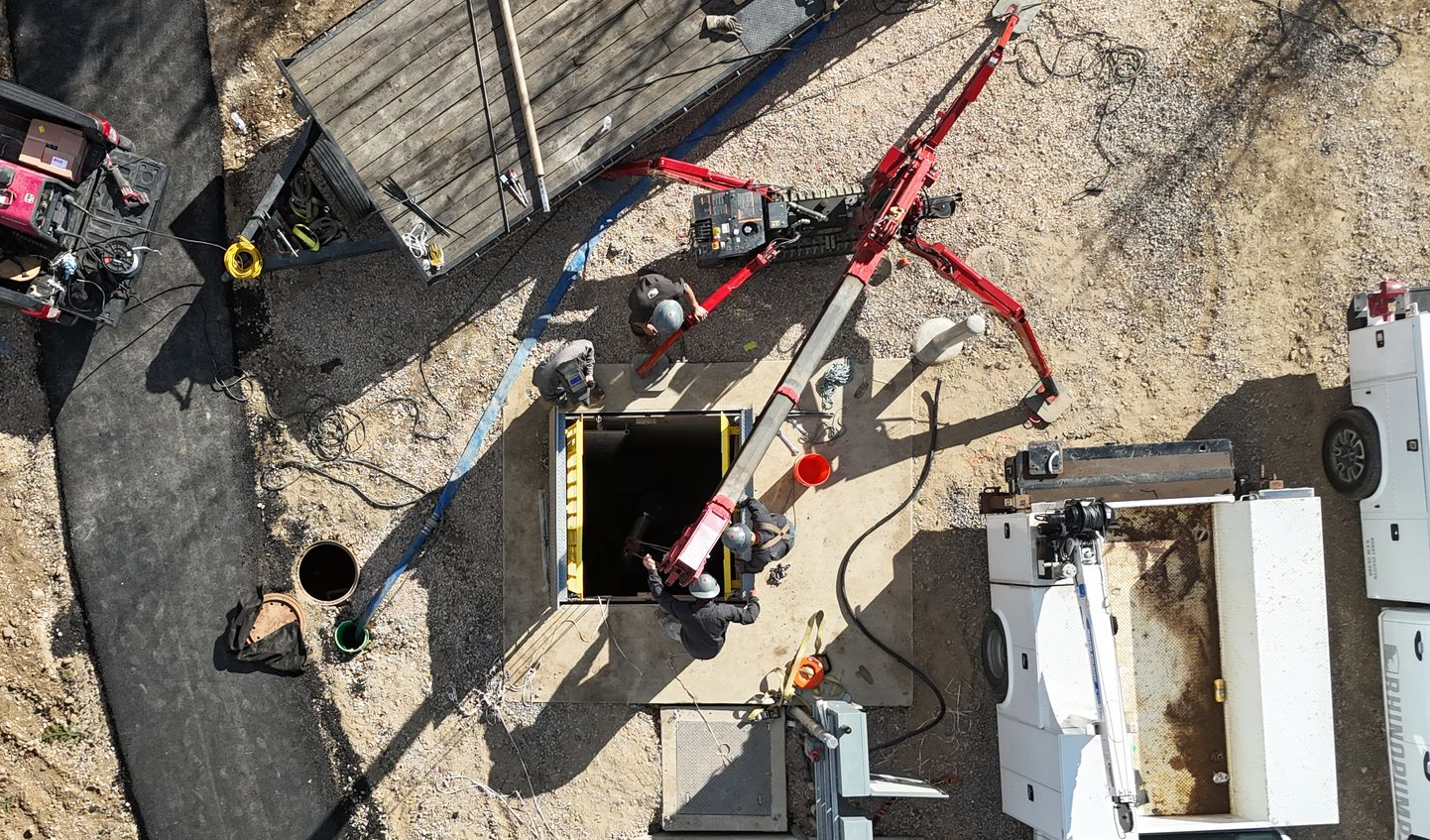 Overhead view of a construction site with workers, red equipment, and a large opening in the ground