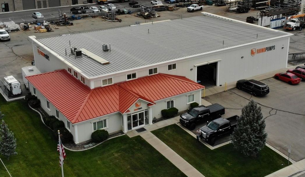 Aerial view of a white commercial building with a red roof and parked cars outside.