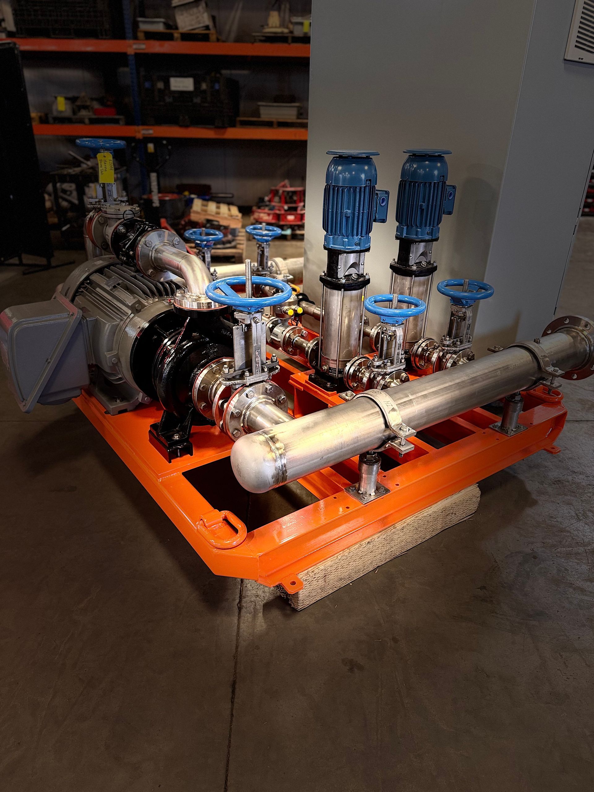 Pump system on an orange skid with blue motors and silver pipes and valves