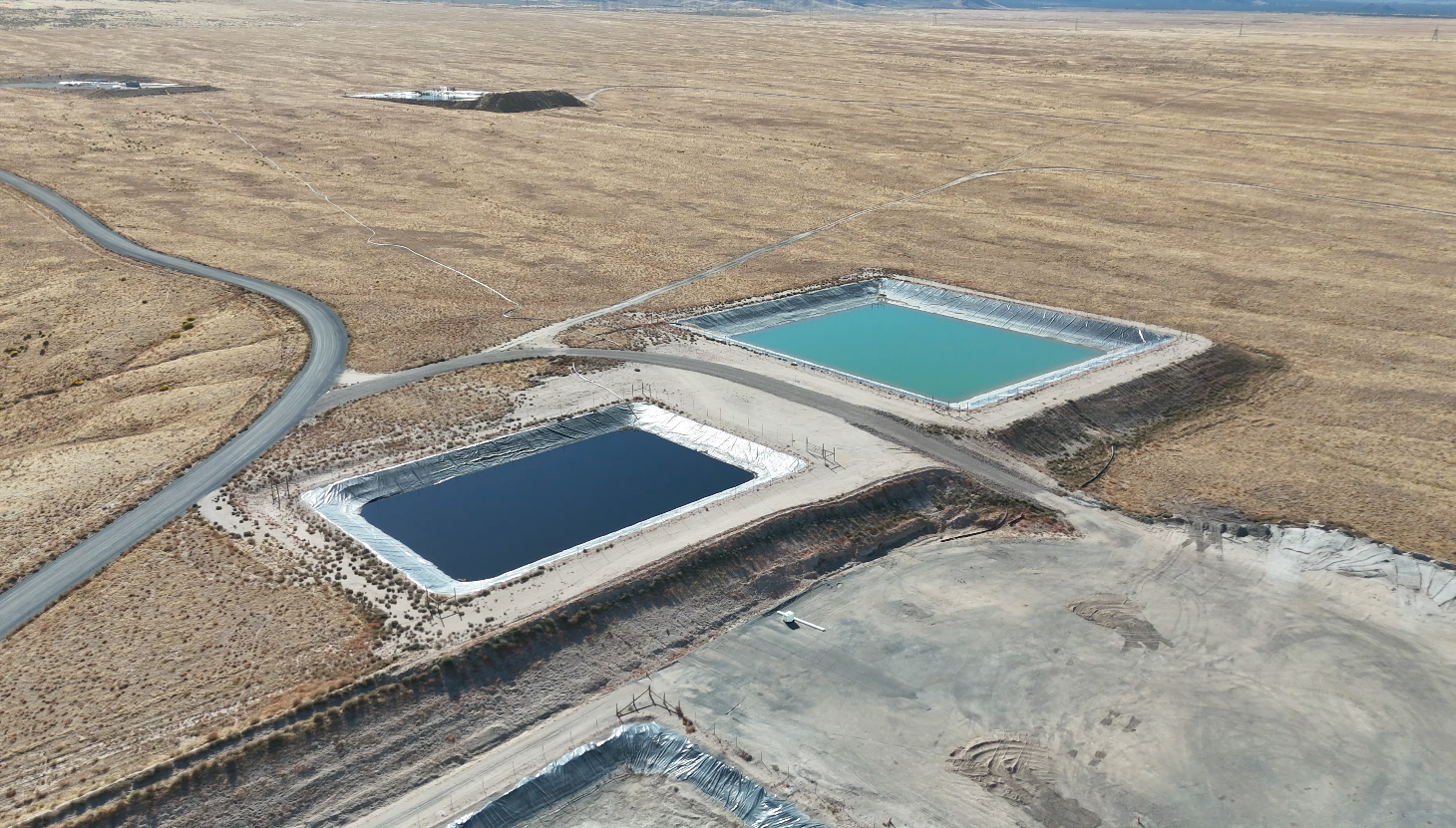 Two rectangular water pools, one blue, one teal, on a brown landscape, a road, and a gravel area.