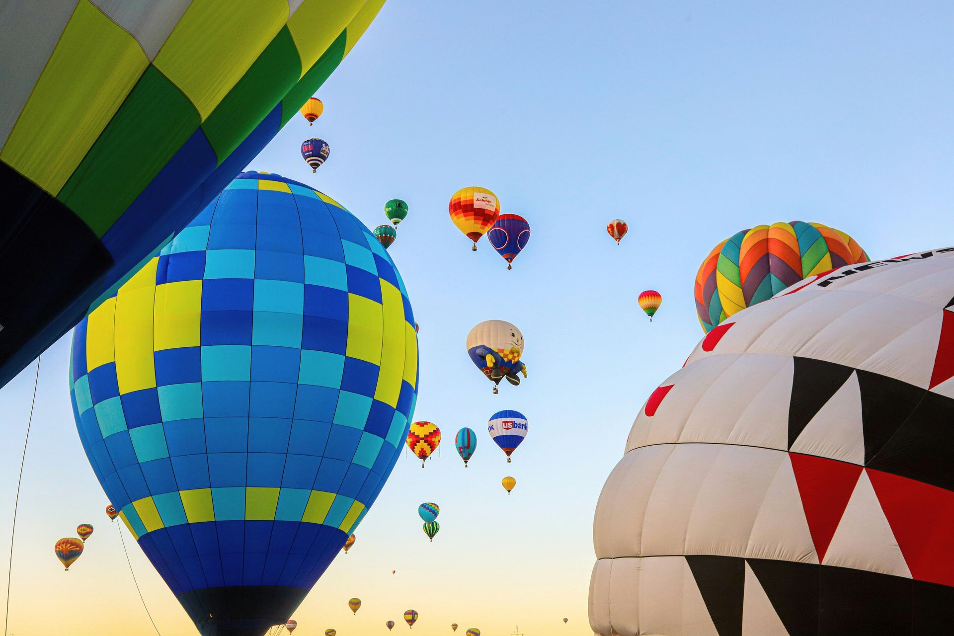 Colorful hot air balloons filling a clear sky, viewed from below during a festival.