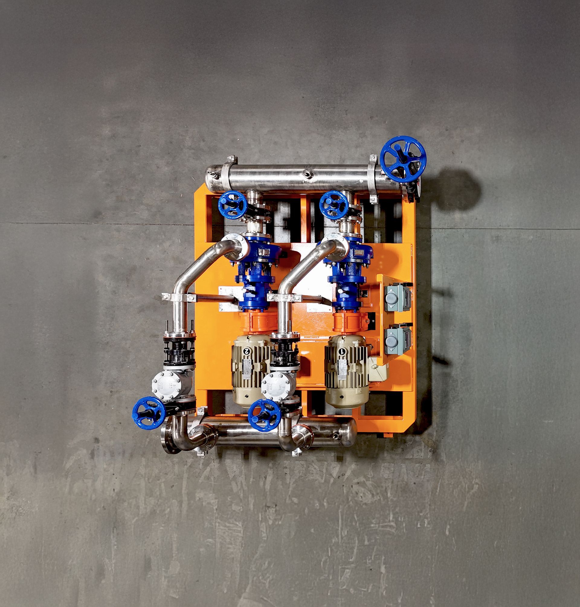 Small industrial machine with blue valves and metal piping mounted on an orange frame against a gray wall