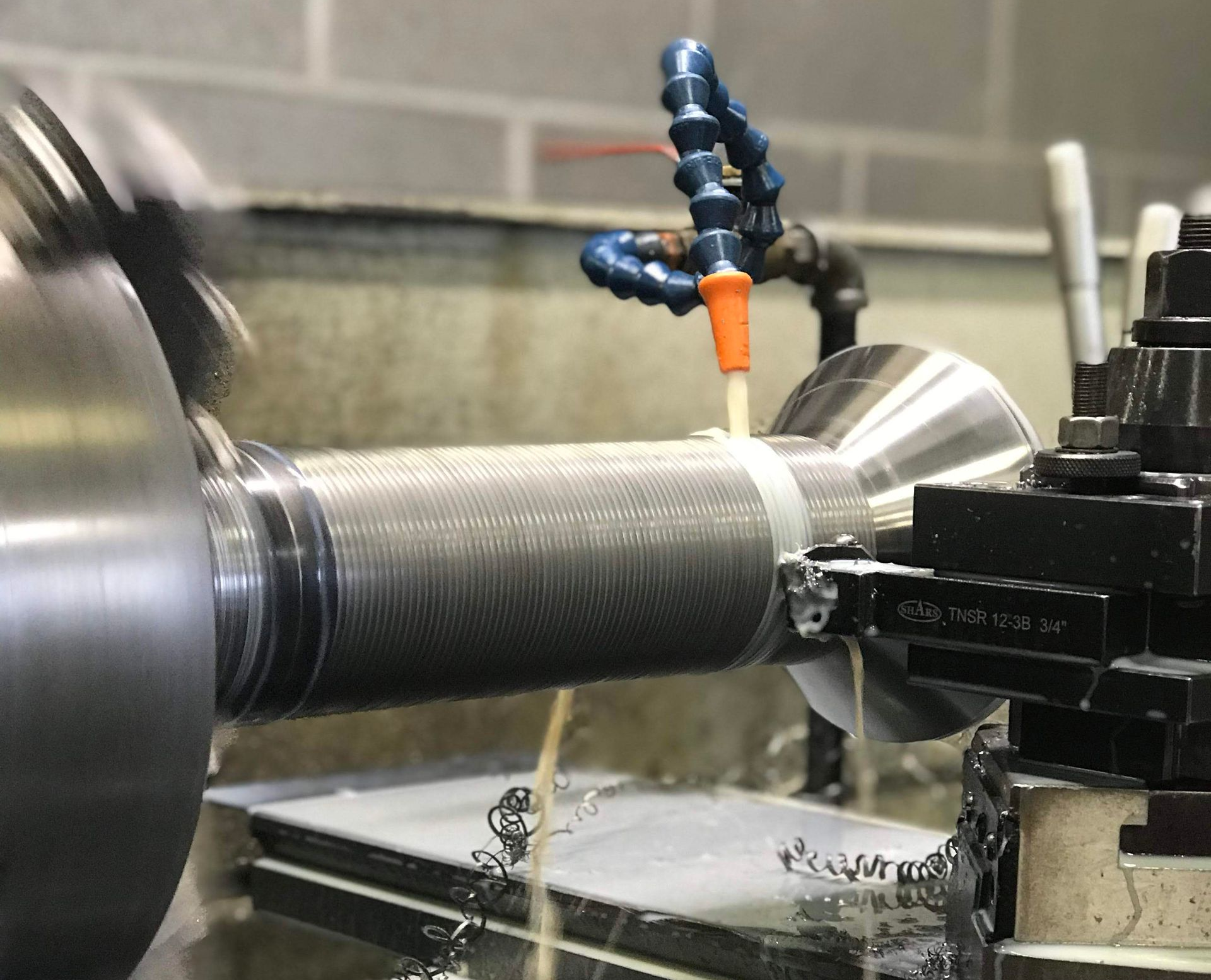 Metal lathe machining a threaded shaft with coolant nozzle spraying from above