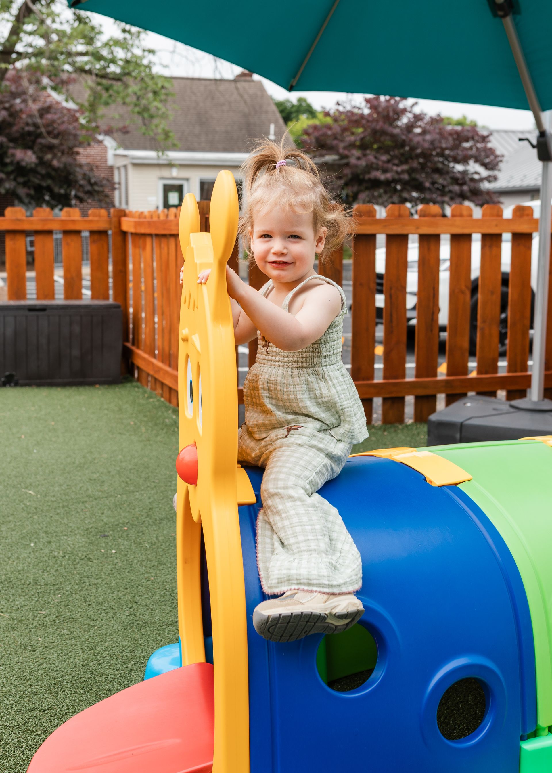 Child playing on colorful playground equipment outdoors under a teal umbrella