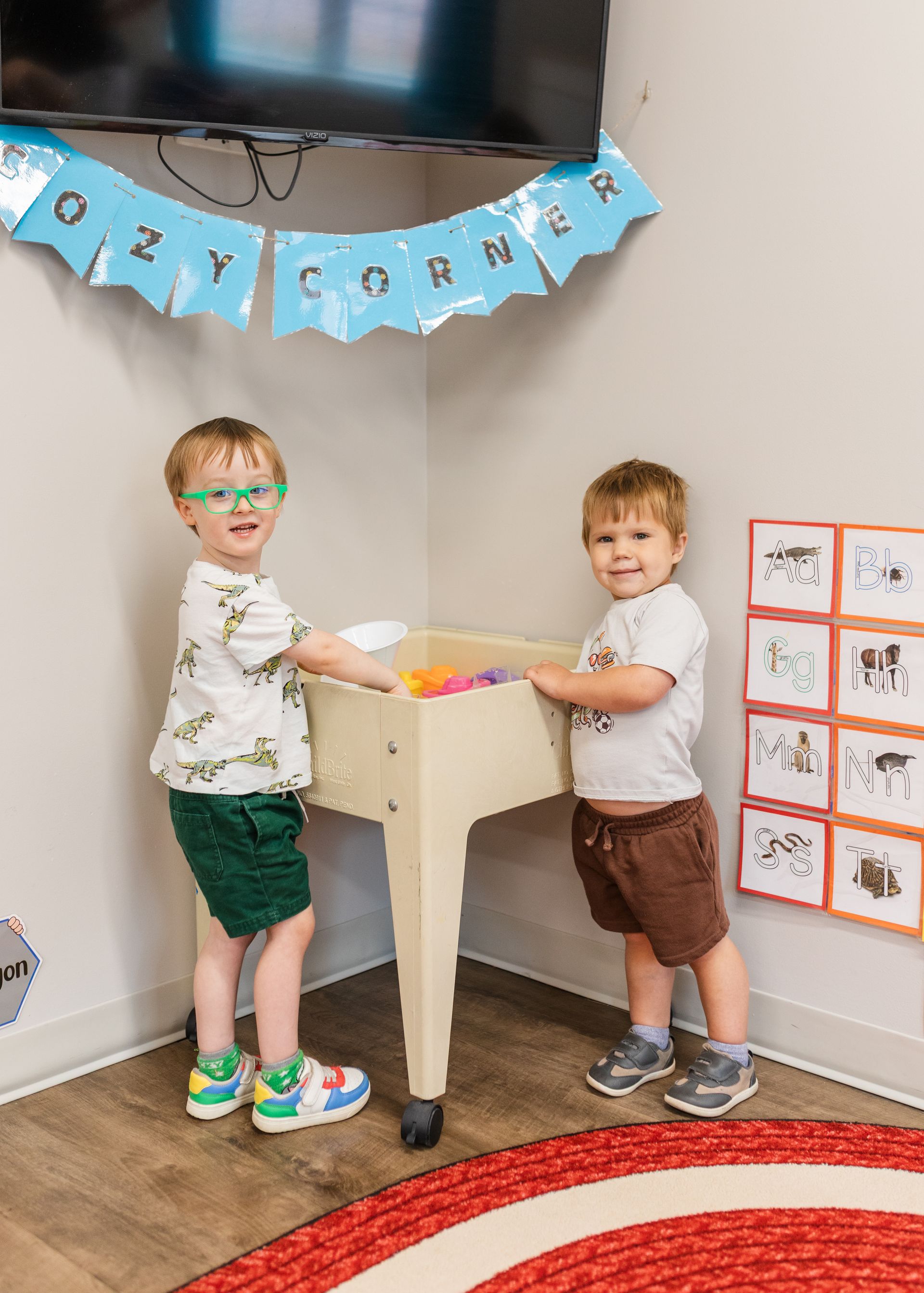 Two children playing at a small table in a decorated room with banners and a red rug