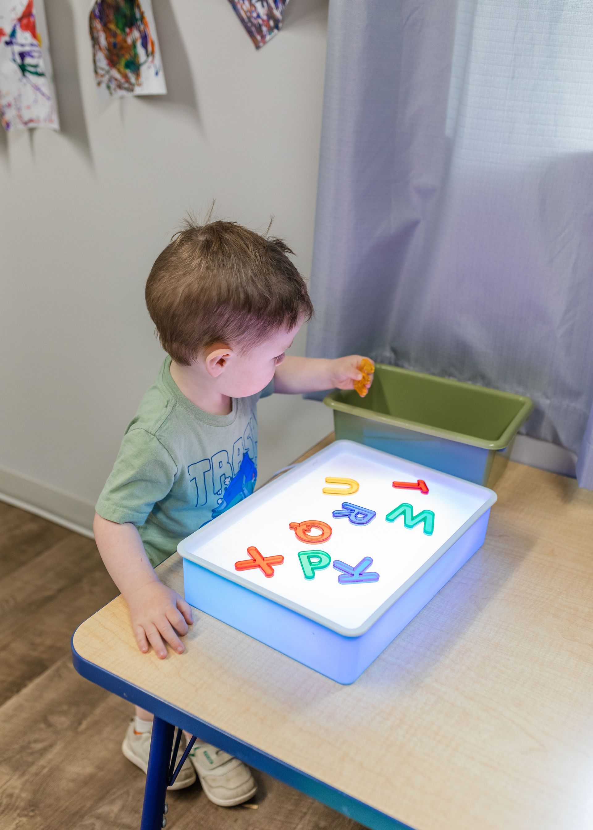 Child at a table playing with colorful letters in a lighted tray