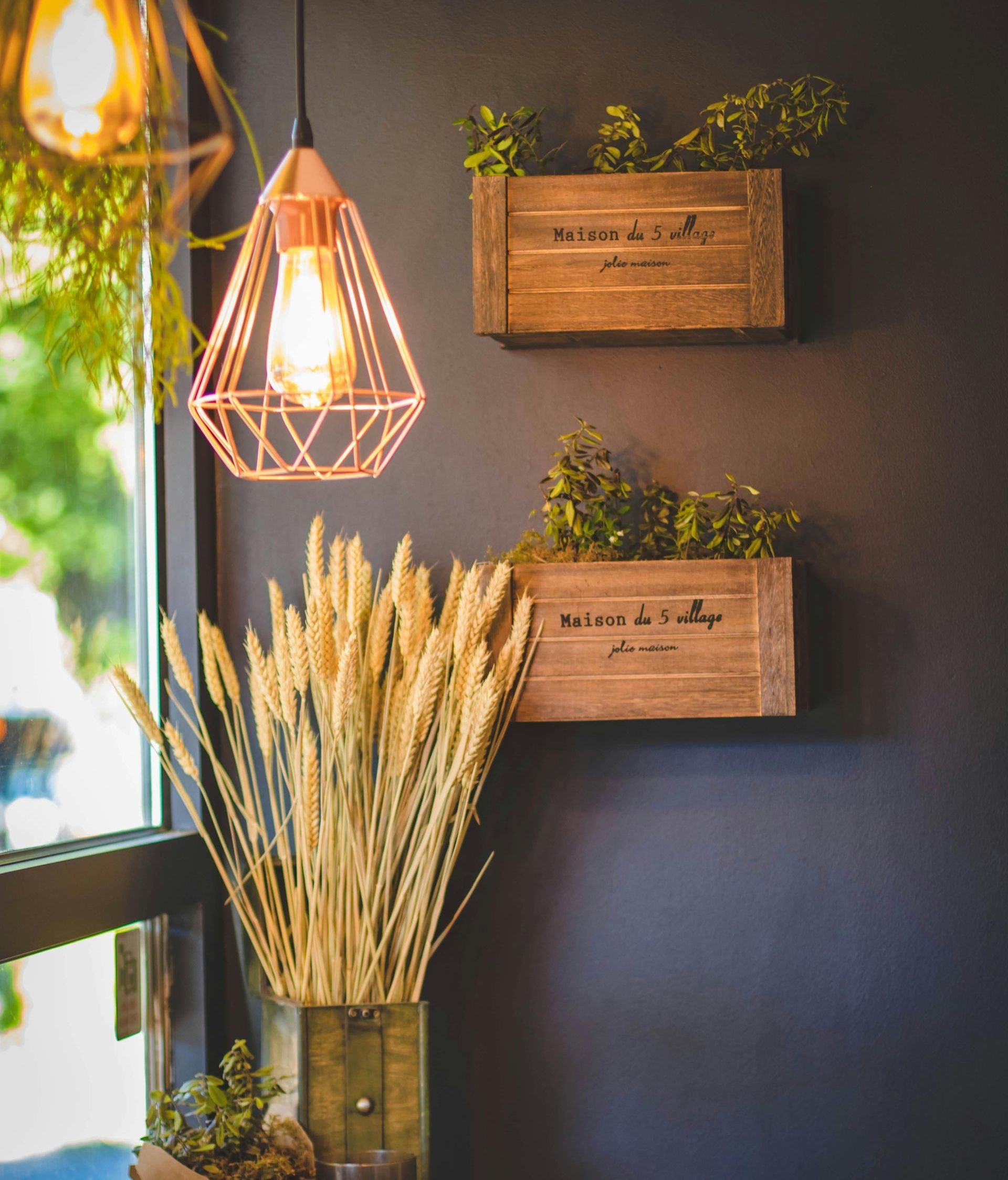 A shelf with three wooden boxes filled with plants and a light hanging from the ceiling.