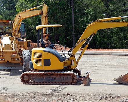 Un homme conduit une excavatrice jaune sur un chantier de construction.