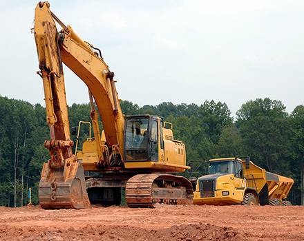 Une excavatrice jaune et un camion à benne jaune sont garés dans un champ de terre.