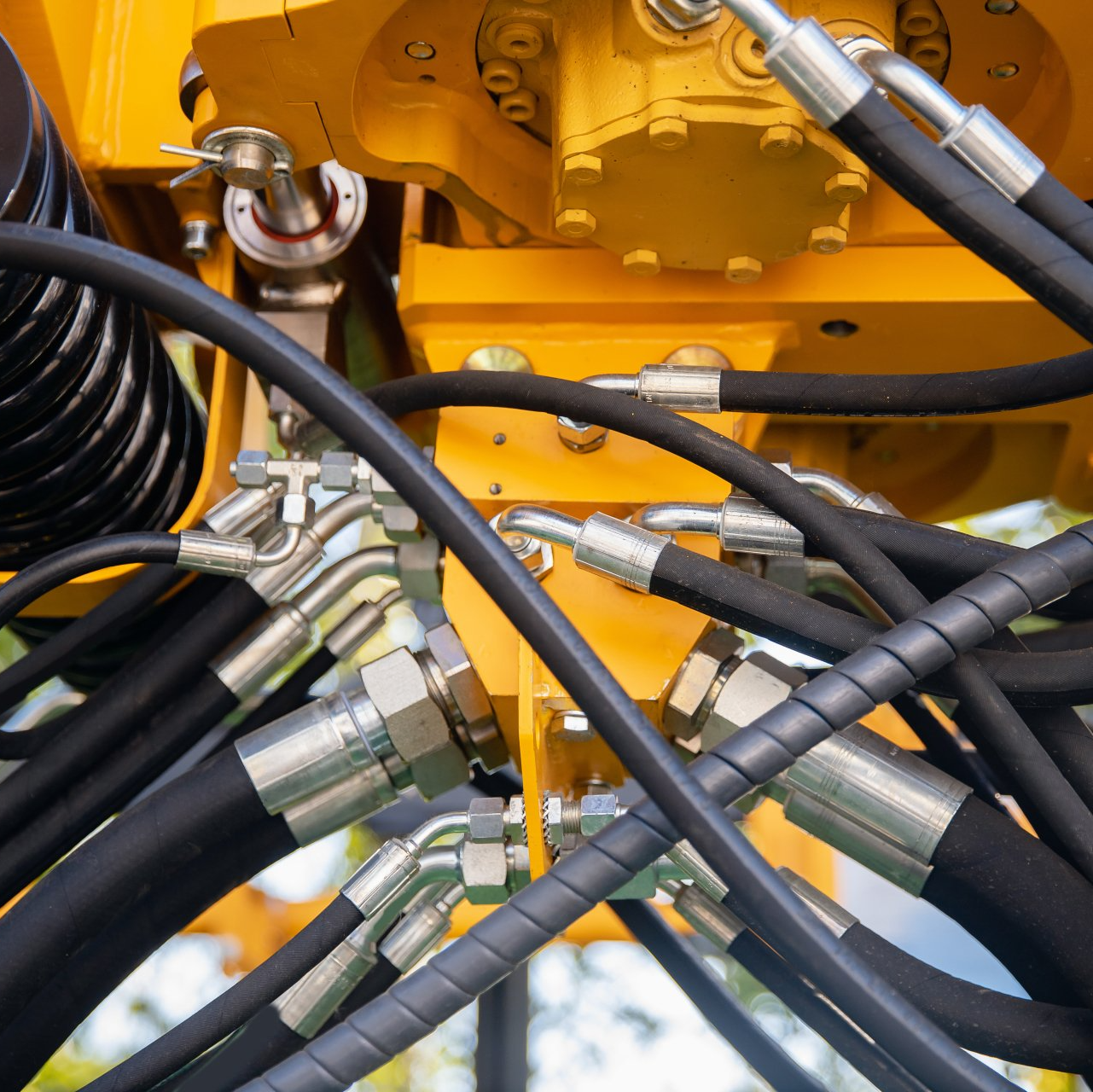 Machine industrielle jaune avec tuyaux hydrauliques noirs et raccords argentés.