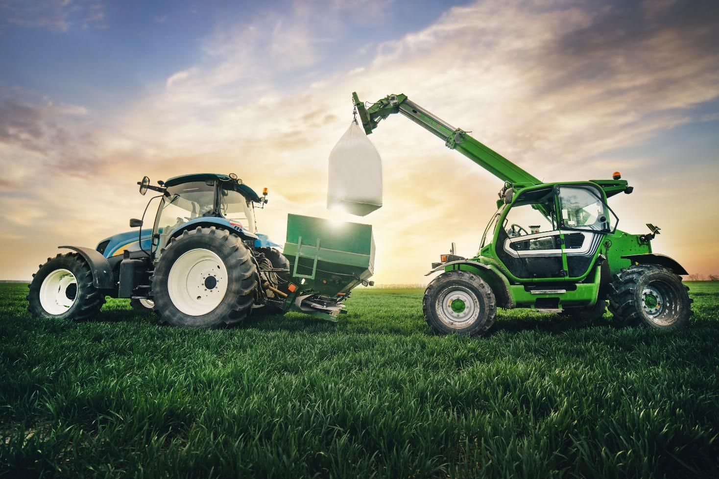 A tractor is loading a bag of hay into a forklift.