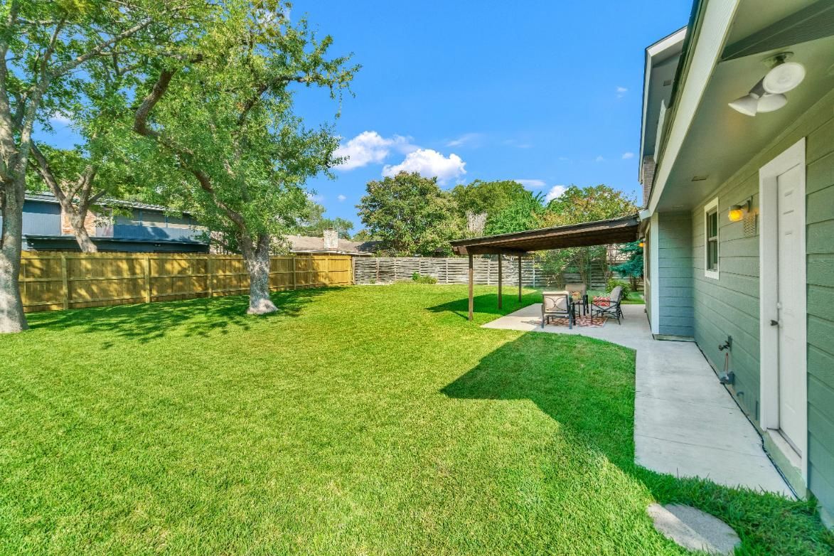 The backyard of a house with a large lawn and a patio area.