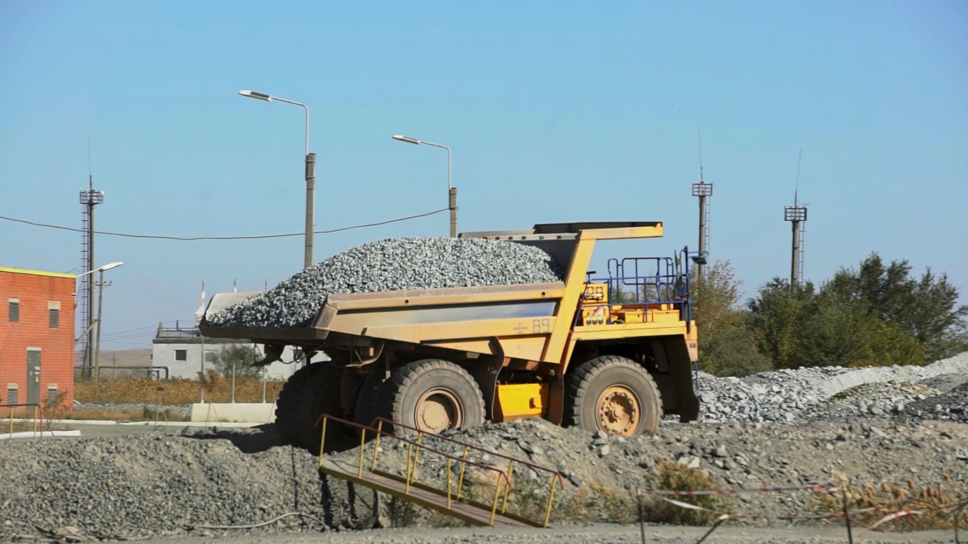 A large yellow dump truck is driving down a dirt road.