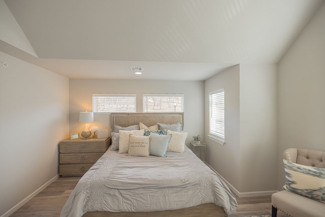 Bedroom with a bed, nightstand, chair, windows, and neutral color palette.