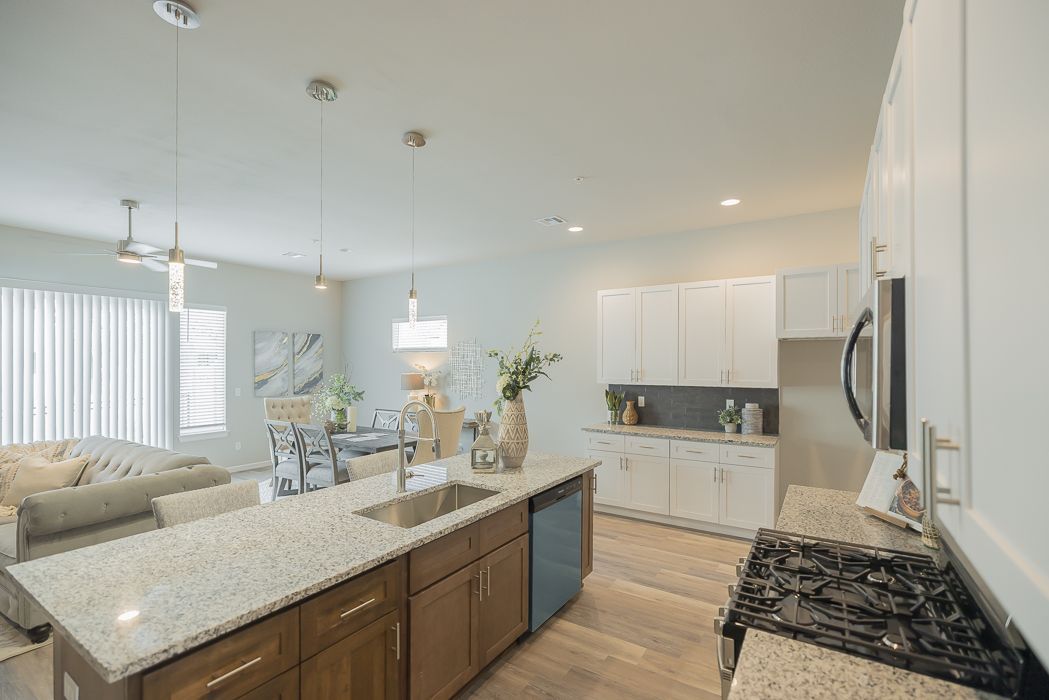 Modern kitchen with island, cabinetry, and living room visible. Bright, neutral colors.