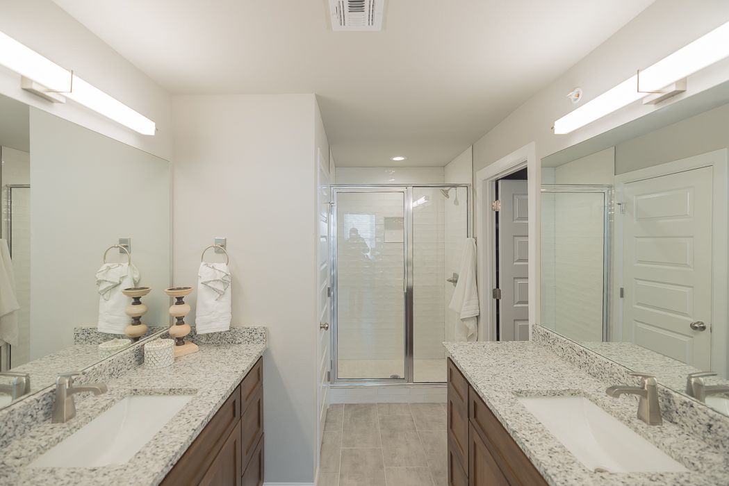 Bathroom with two sinks, mirrors, and a shower, featuring light granite countertops and wood cabinets.