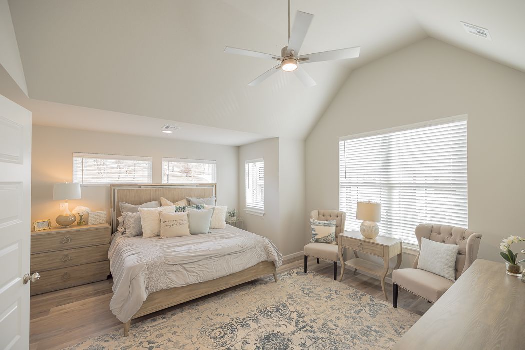 Bedroom with bed, two chairs, and dresser; white walls, light-colored furniture, patterned rug.