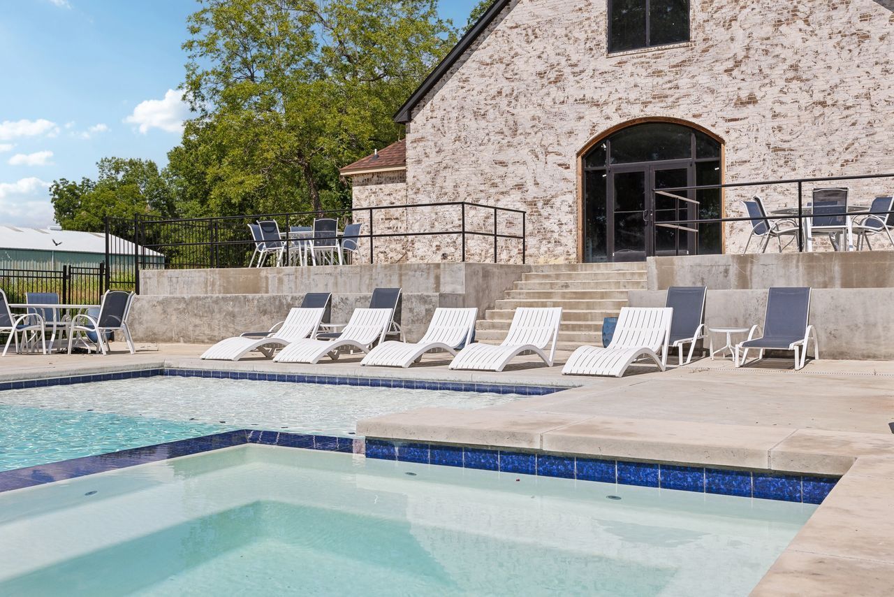 A pool with lounge chairs in front of a stone building under a blue sky.