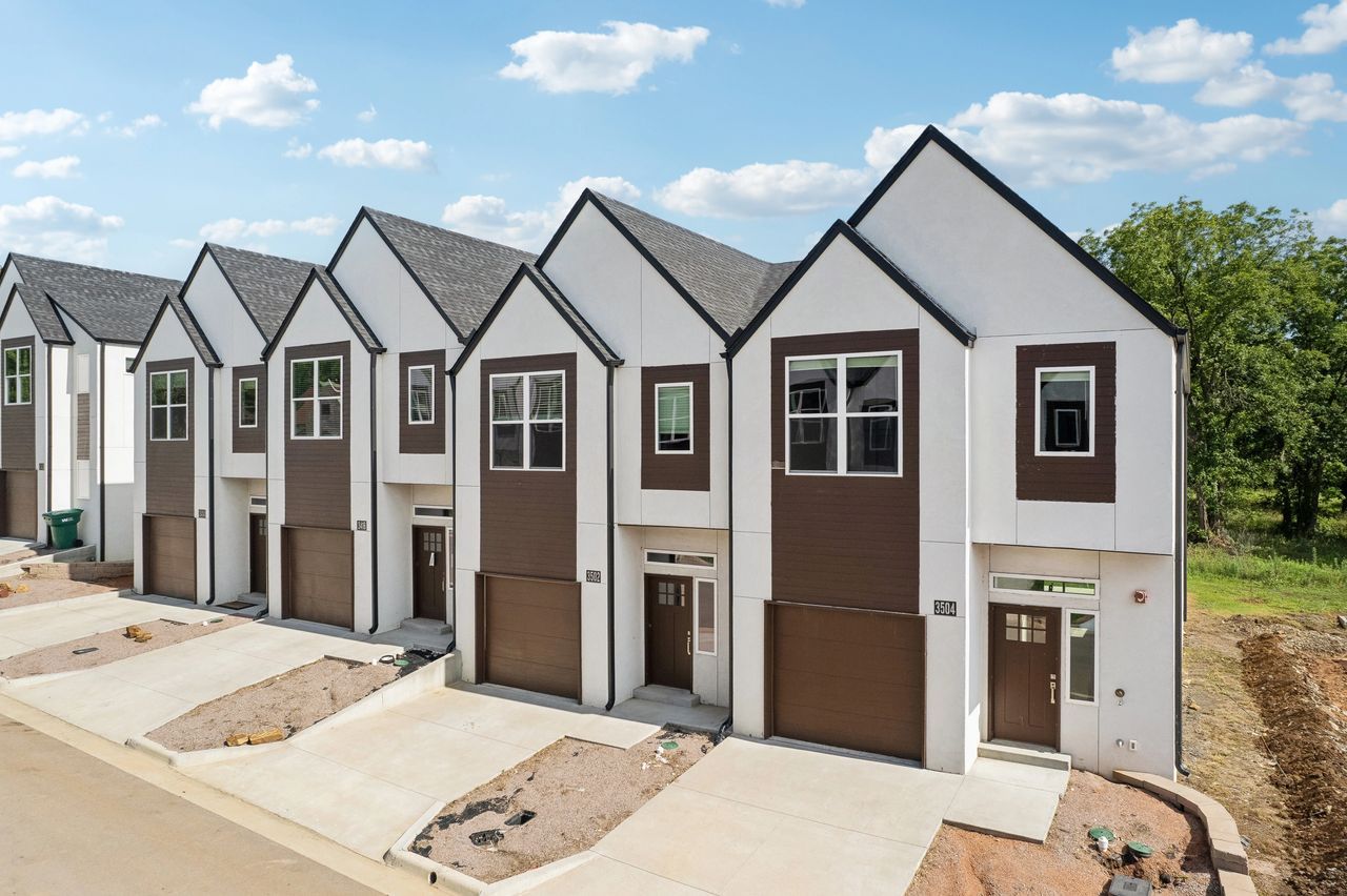 Row of modern townhomes with white exteriors, brown accents, and garages.