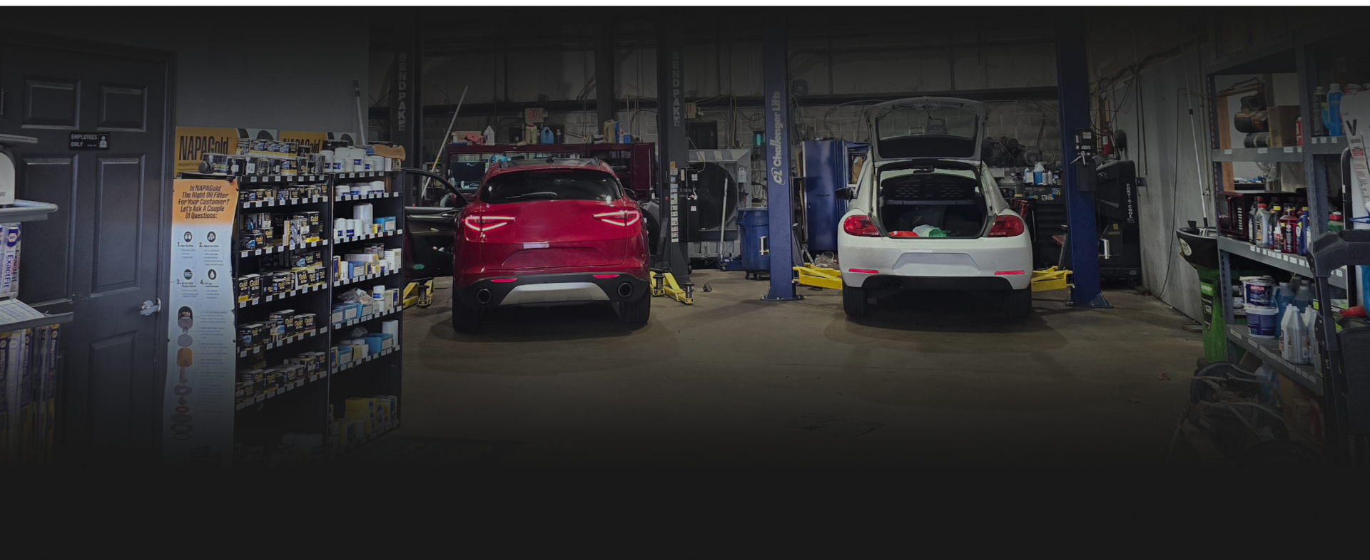 Inside a garage, a red car and a white car are being worked on. | Integrity Auto Repair