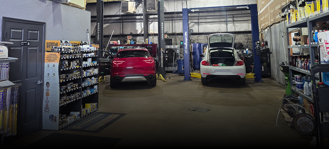 Inside a car repair shop, two cars between auto lifts, shelves of parts, open doors. | Integrity Auto Repair