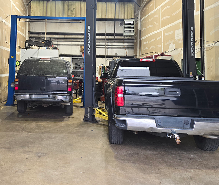 Two black vehicles inside an auto repair shop, on lifts. | Integrity Auto Repair