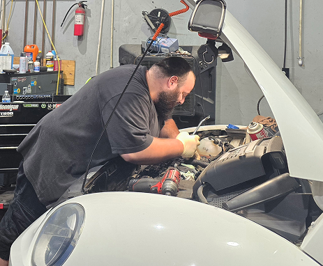 Mechanic working on a white car engine in a garage. He's wearing gloves and using tools. | Integrity Auto Repair